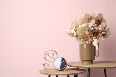 Photo of Stylish ceramic vase with dry flowers and leaves on wooden table near pink wall. Space for text