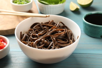 Photo of Tasty buckwheat noodles (soba) served on light blue wooden table, closeup