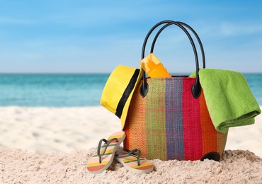 Stylish bag with different accessories on sandy beach near ocean, space for text 