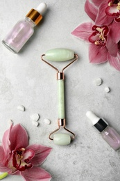 Photo of Natural jade face roller, cosmetic product and flowers on grey background, flat lay