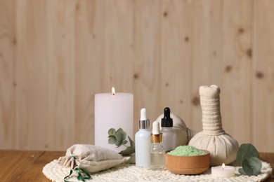 Photo of Different aromatherapy products, burning candles and eucalyptus leaves on wooden table, space for text