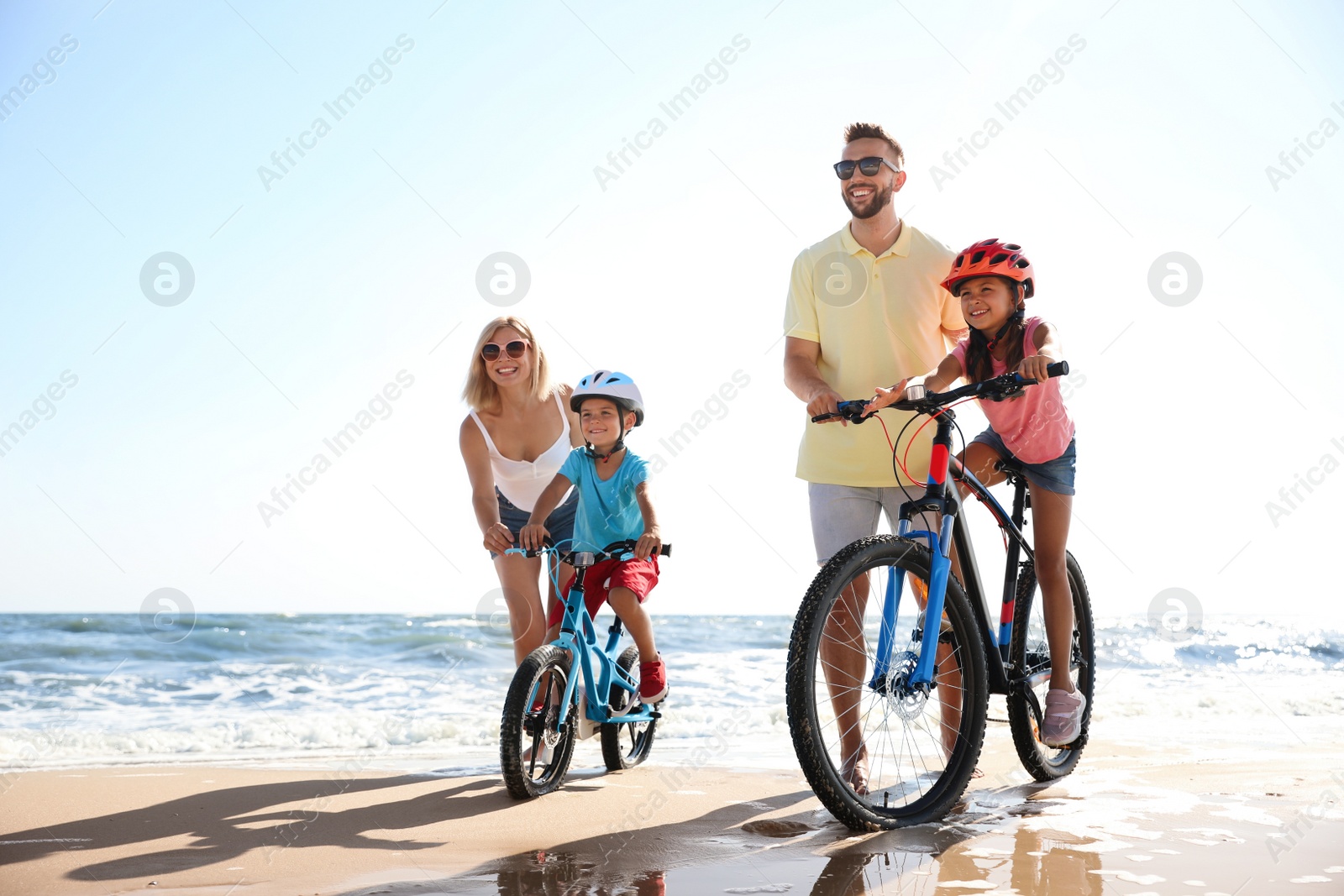 Photo of Happy parents teaching children to ride bicycles on sandy beach near sea