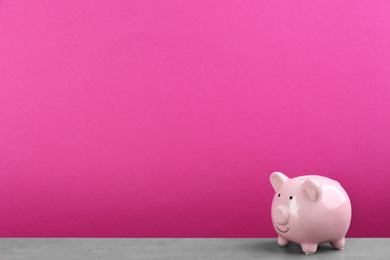 Piggy bank on light grey table against pink background. Space for text