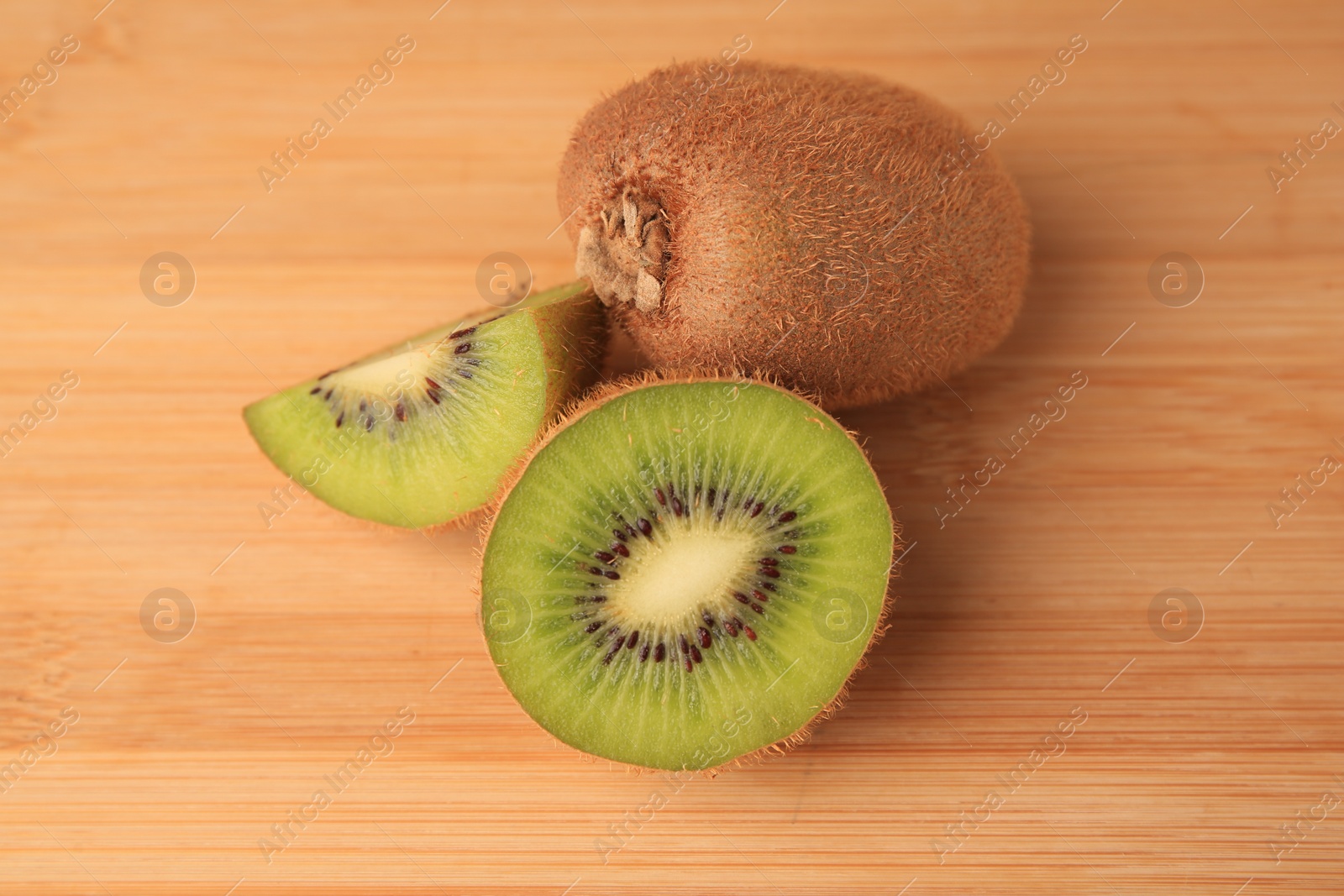 Photo of Whole and cut kiwis on wooden table, closeup