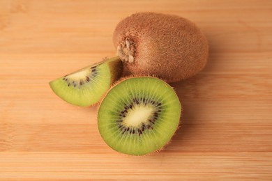 Photo of Whole and cut kiwis on wooden table, closeup