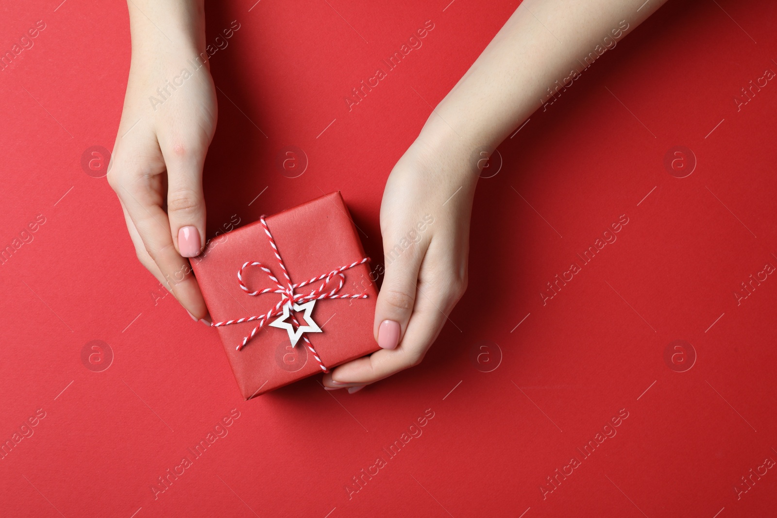 Photo of Woman with beautifully wrapped Christmas gift box on red background, top view