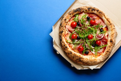 Tasty pizza with meat and arugula in cardboard box on blue background, top view. Space for text