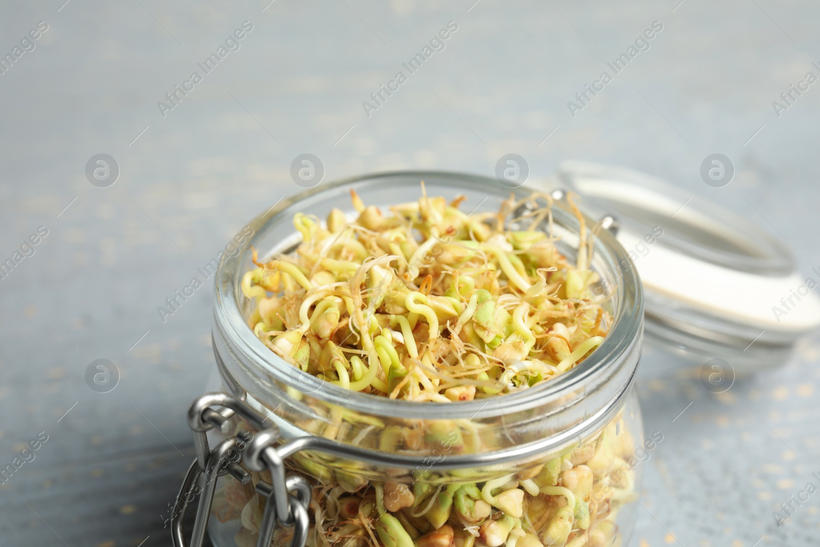 Photo of Glass jar with sprouted green buckwheat on grey wooden table, closeup