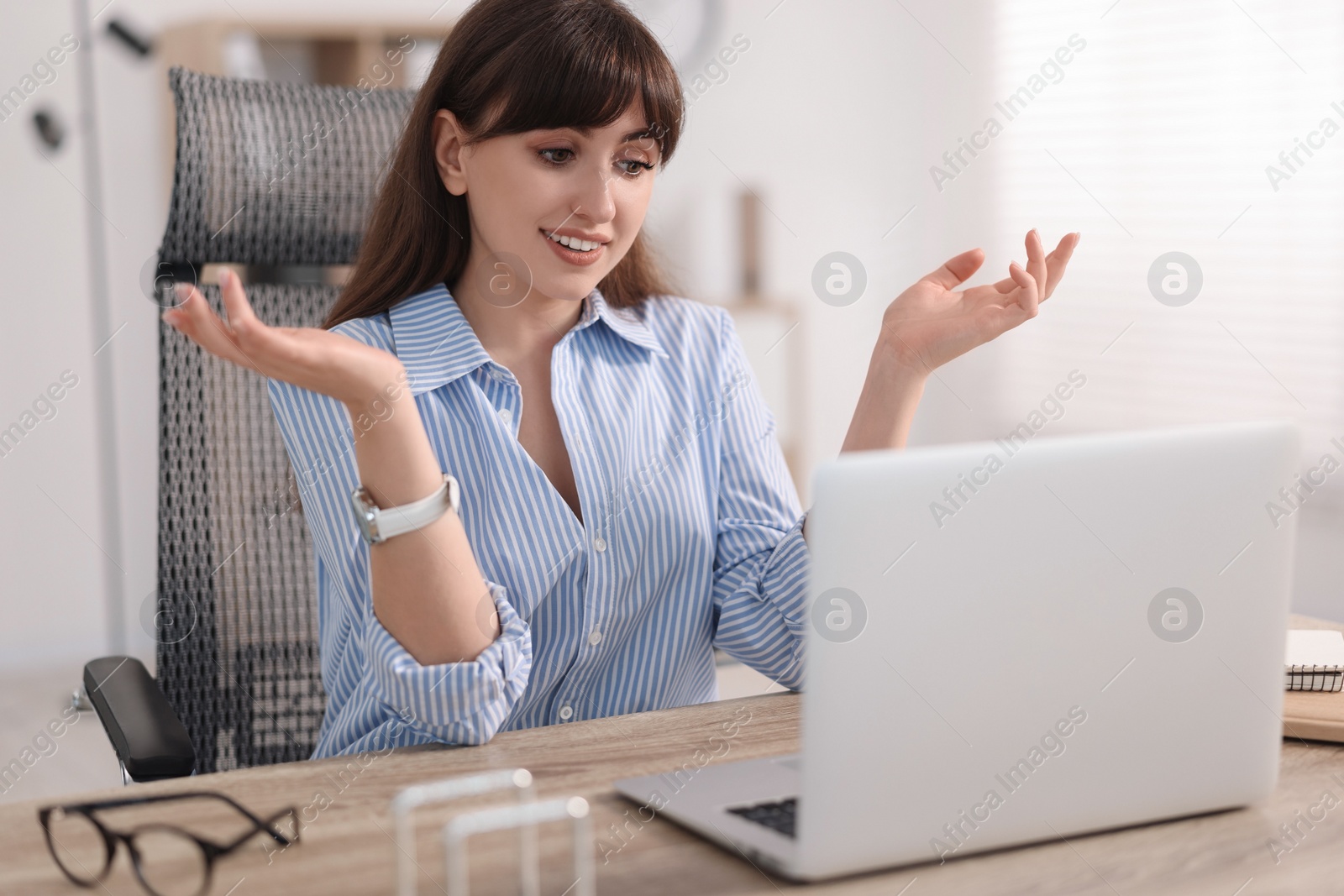 Photo of Woman using video chat during webinar at wooden table in office