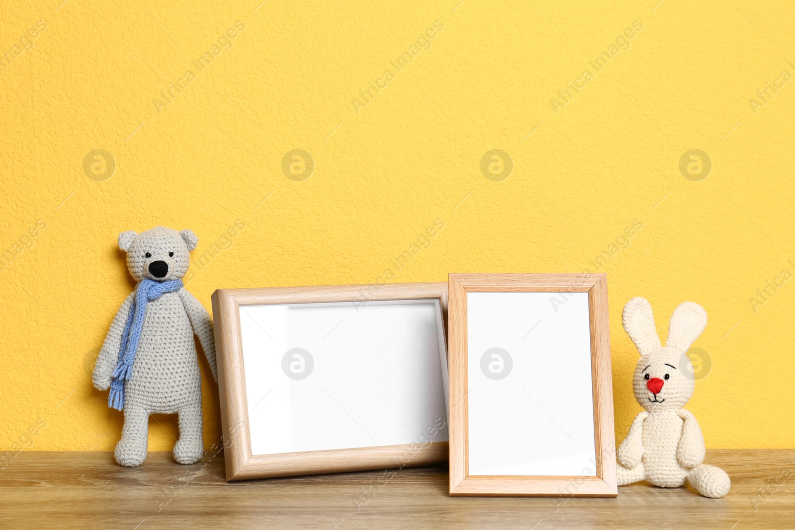 Photo of Soft toys and photo frames on table against yellow background, space for text. Child room interior