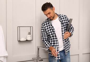 Photo of Plumber with clipboard checking water tap in bathroom