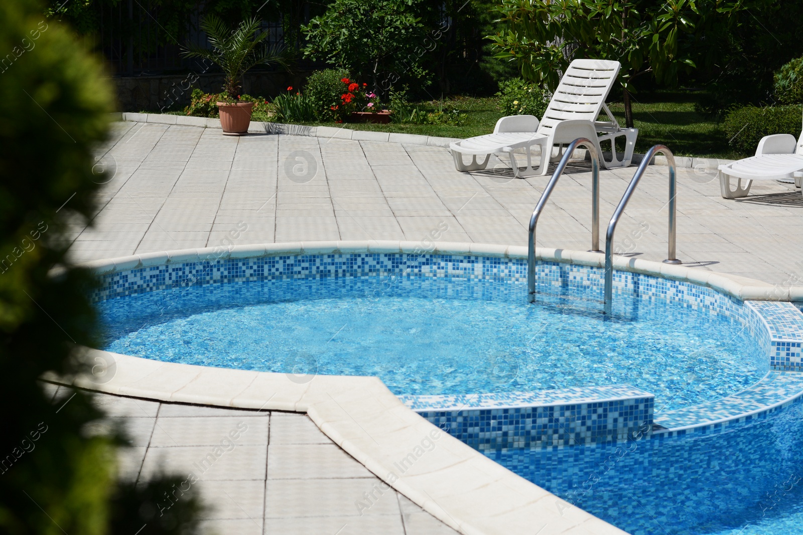 Photo of Outdoor swimming pool with handrails and empty sunbeds at resort on sunny day