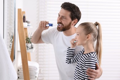 Father and his daughter brushing teeth together near mirror in bathroom