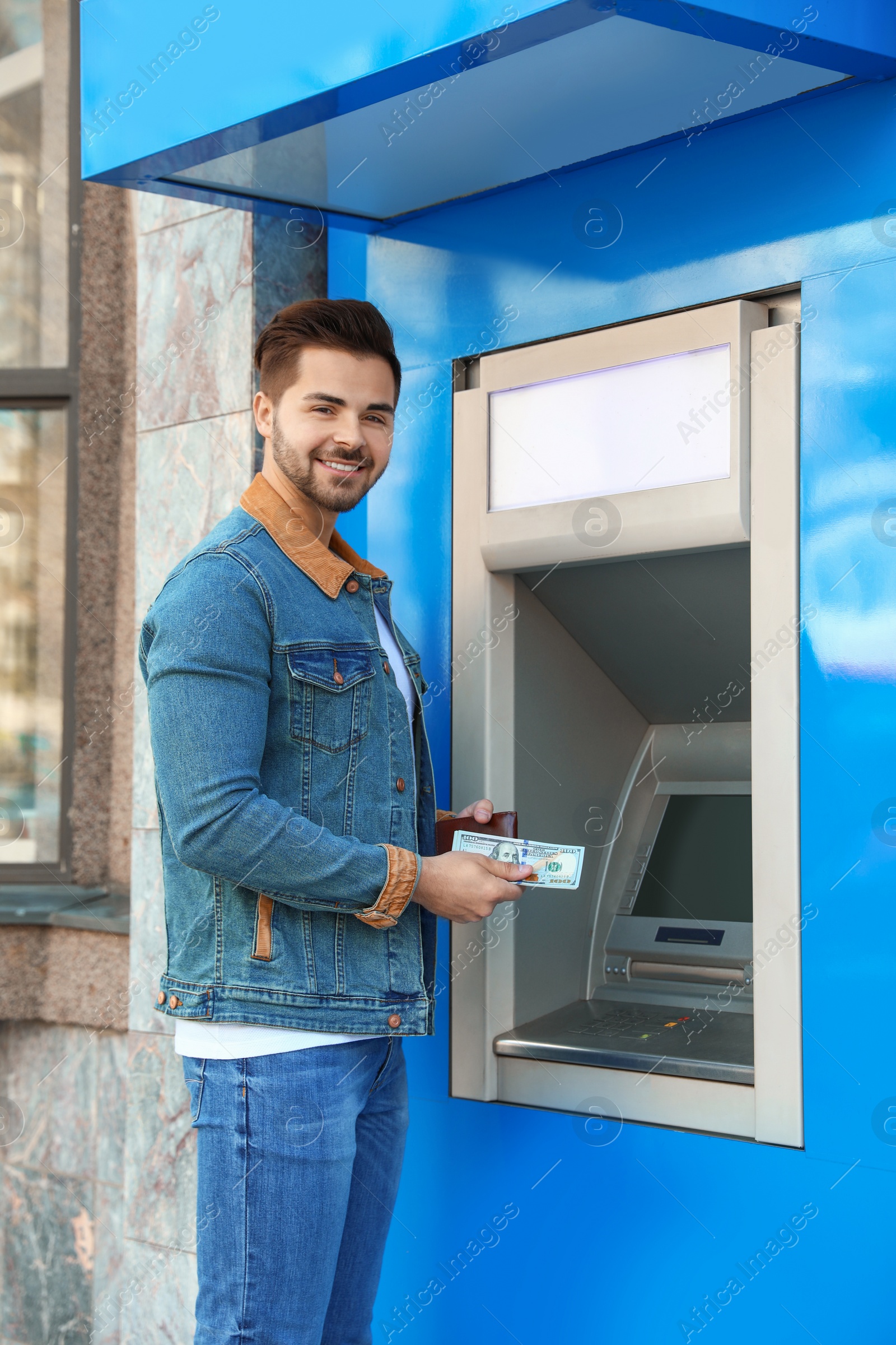 Photo of Young man with money near cash machine outdoors