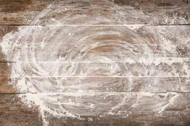 Photo of Scattered flour on wooden table, top view