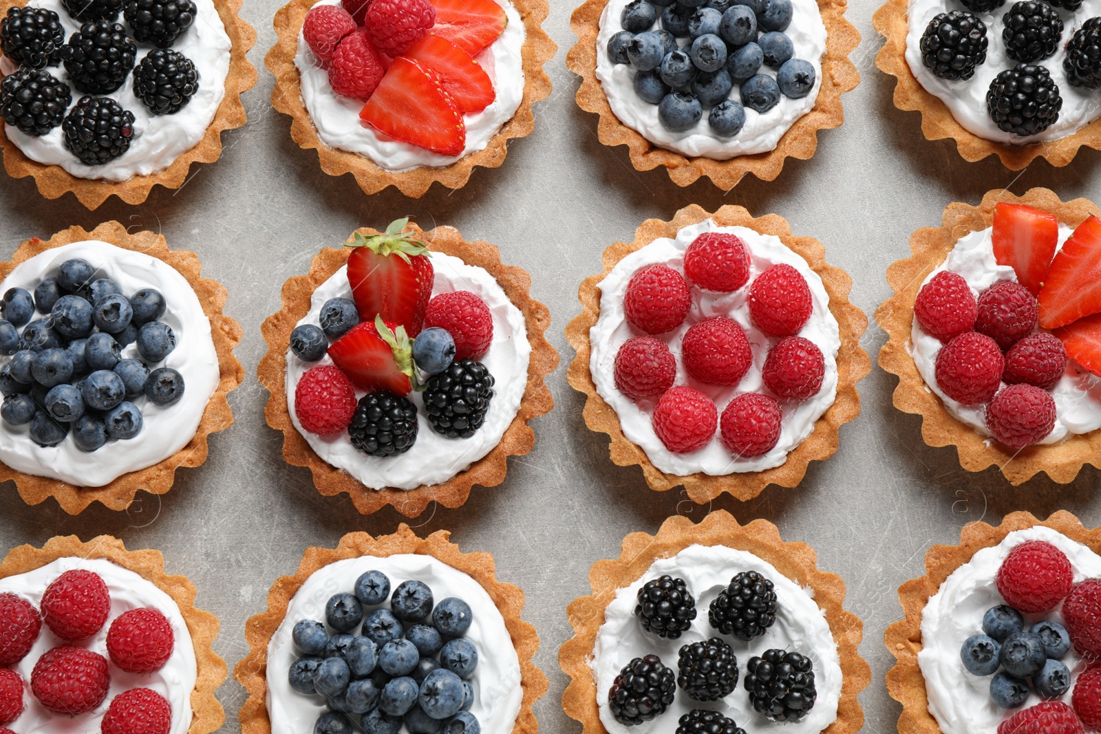 Photo of Different berry tarts on table, flat lay. Delicious pastries