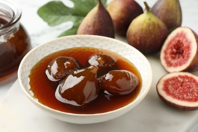 Photo of Bowl of tasty sweet jam and fresh figs on white marble table