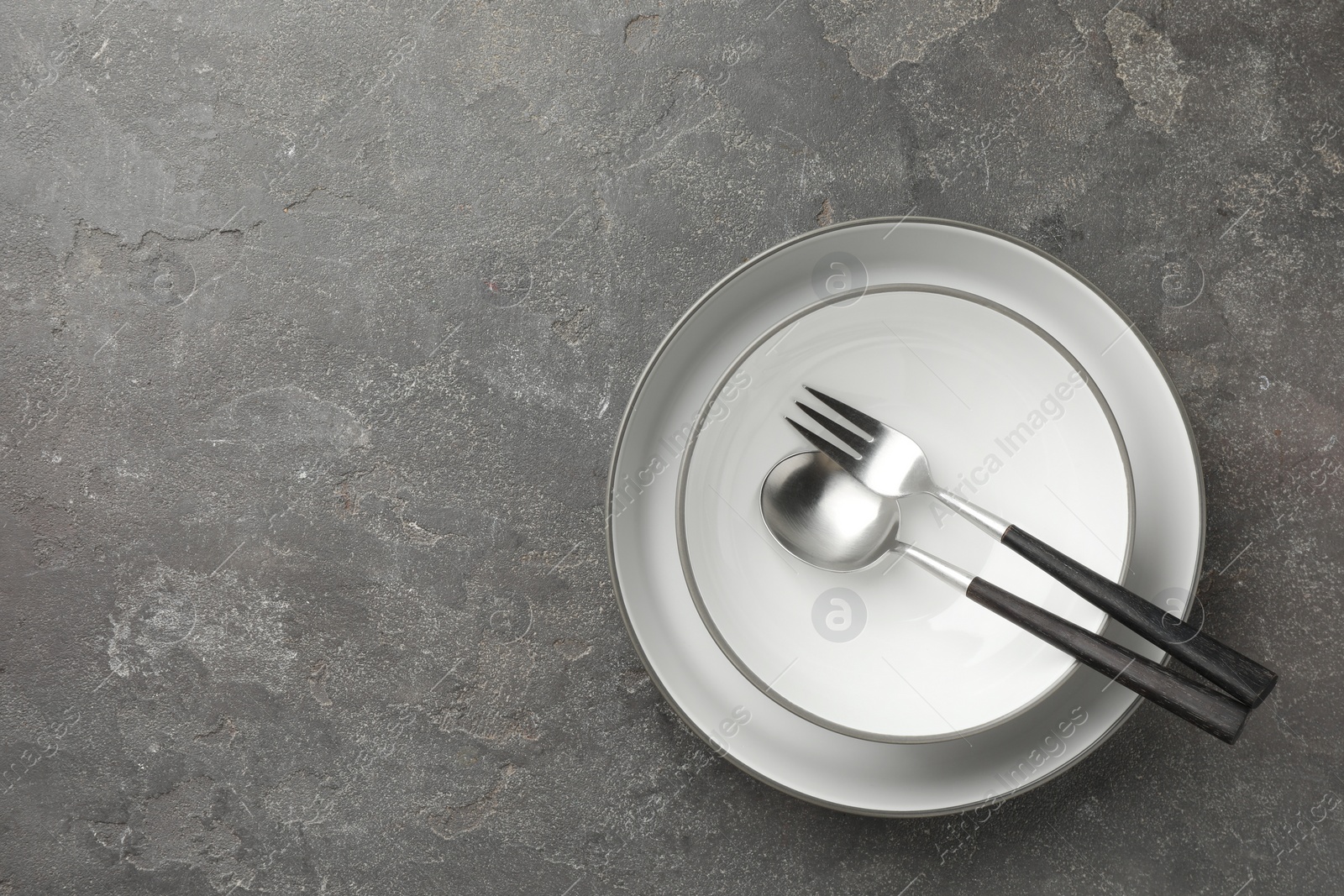 Photo of Stylish setting with cutlery and plates on grey textured table, top view. Space for text