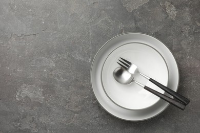 Stylish setting with cutlery and plates on grey textured table, top view. Space for text