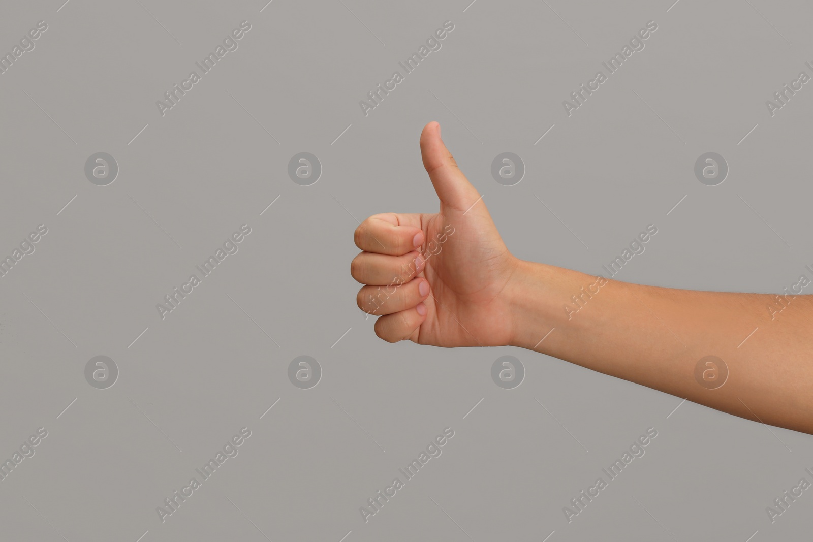 Photo of Teenage boy showing thumb up on light background, closeup