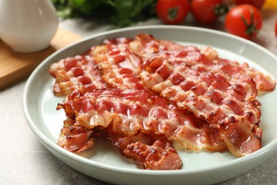 Photo of Plate with fried bacon slices on grey textured table, closeup