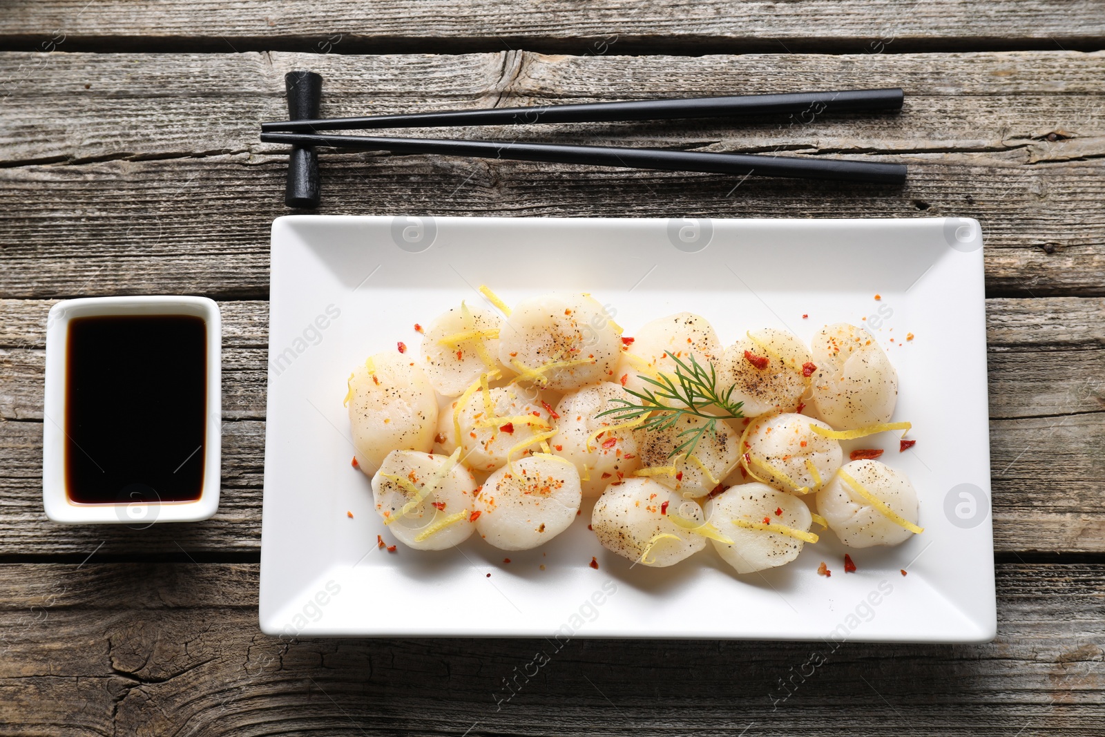 Photo of Raw scallops with spices, dill, lemon zest and soy sauce on wooden table, flat lay