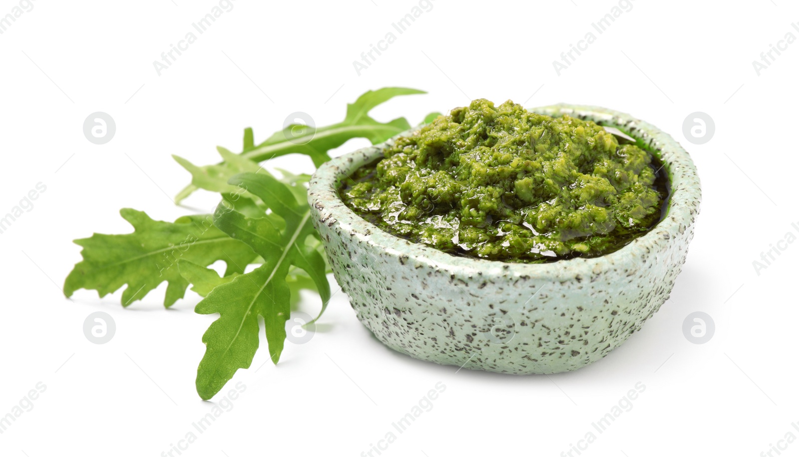 Photo of Bowl of tasty pesto and arugula on white background