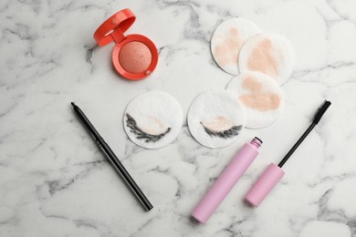 Photo of Dirty cotton pads and cosmetic products on white marble background, flat lay