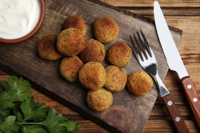 Photo of Delicious falafel balls with parsley and sauce on wooden table, flat lay