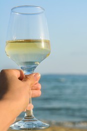Photo of Woman holding glass of tasty wine near sea, closeup. Space for text