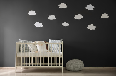 Photo of Cute baby room interior with modern crib near decorative clouds on dark wall