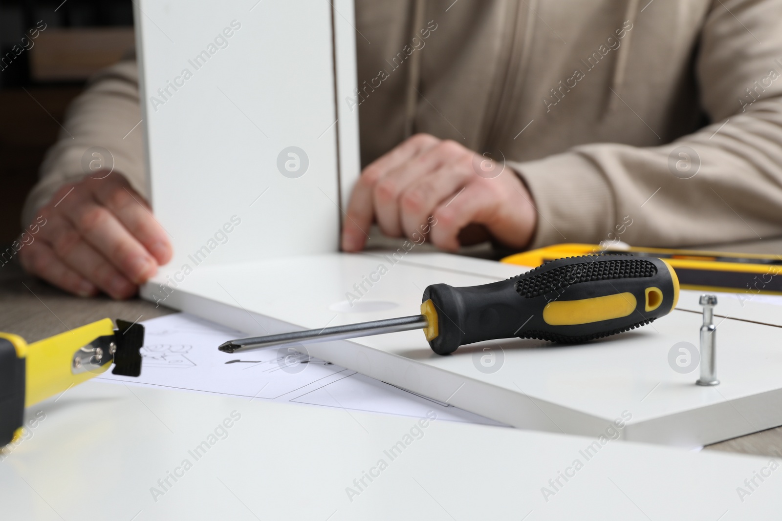 Photo of Man assembling wooden furniture at table, focus on screwdriver