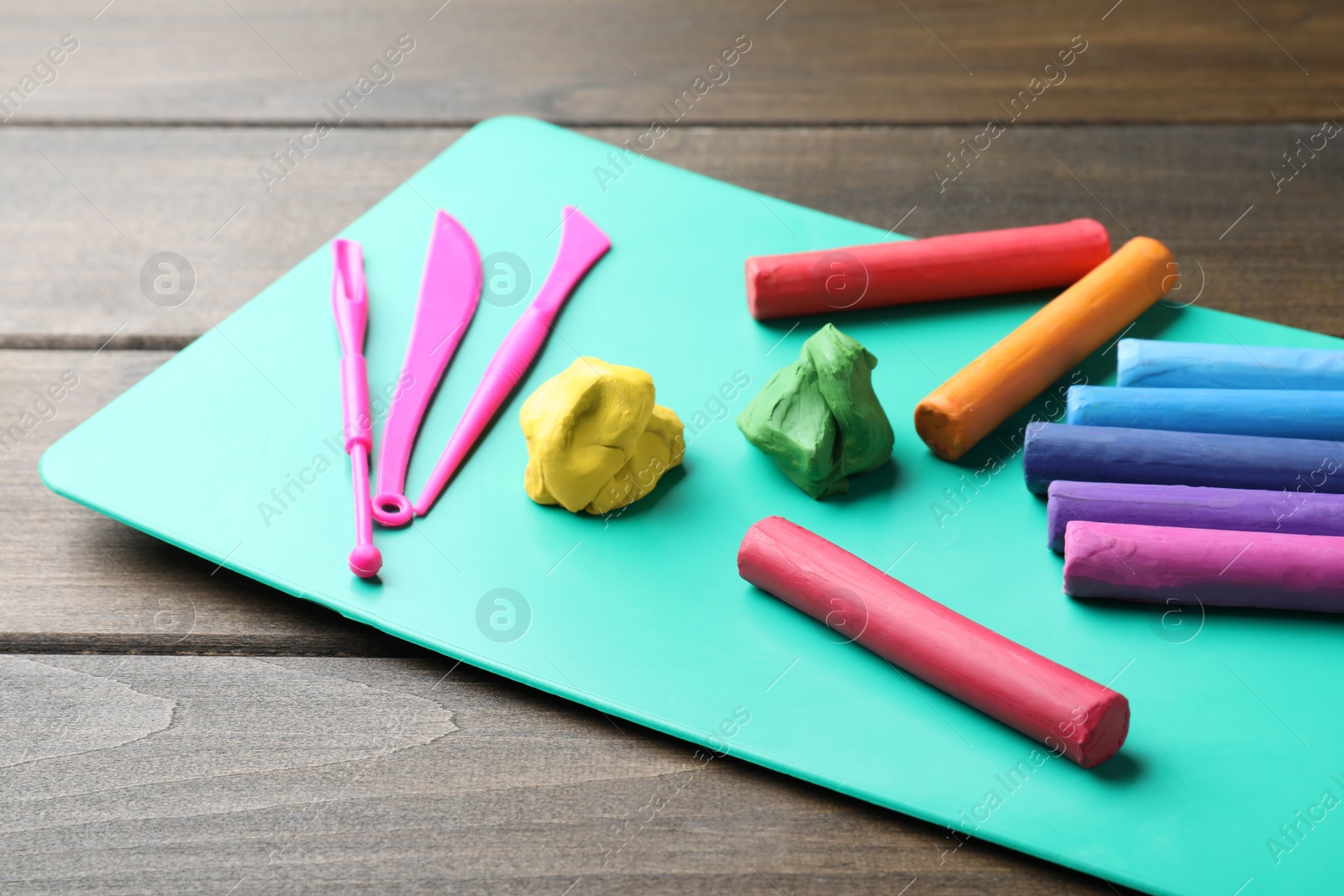 Photo of Many different colorful plasticine pieces with tools on wooden table