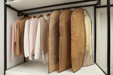 Photo of Garment bags with clothes on rack in dressing room