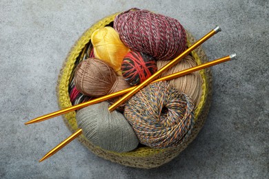 Soft woolen yarns and knitting needles on grey table, top view