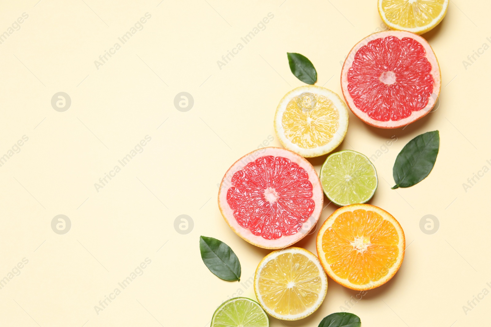 Photo of Different cut citrus fruits and leaves on beige table, flat lay. Space for text