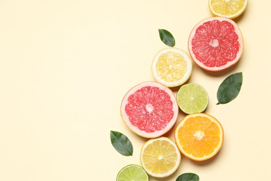 Different cut citrus fruits and leaves on beige table, flat lay. Space for text