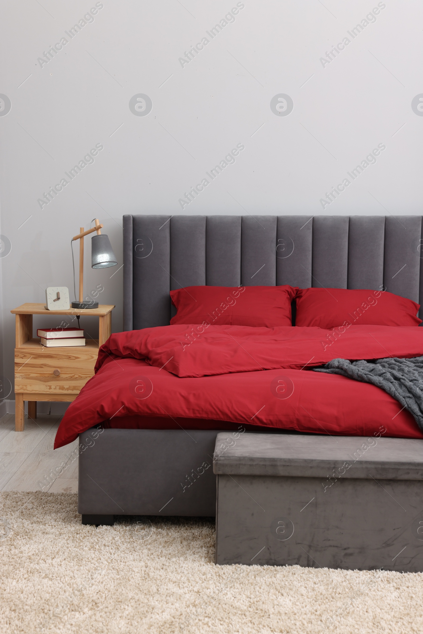 Photo of Comfortable bed, lamp, alarm clock and books on wooden bedside table in bedroom. Interior design