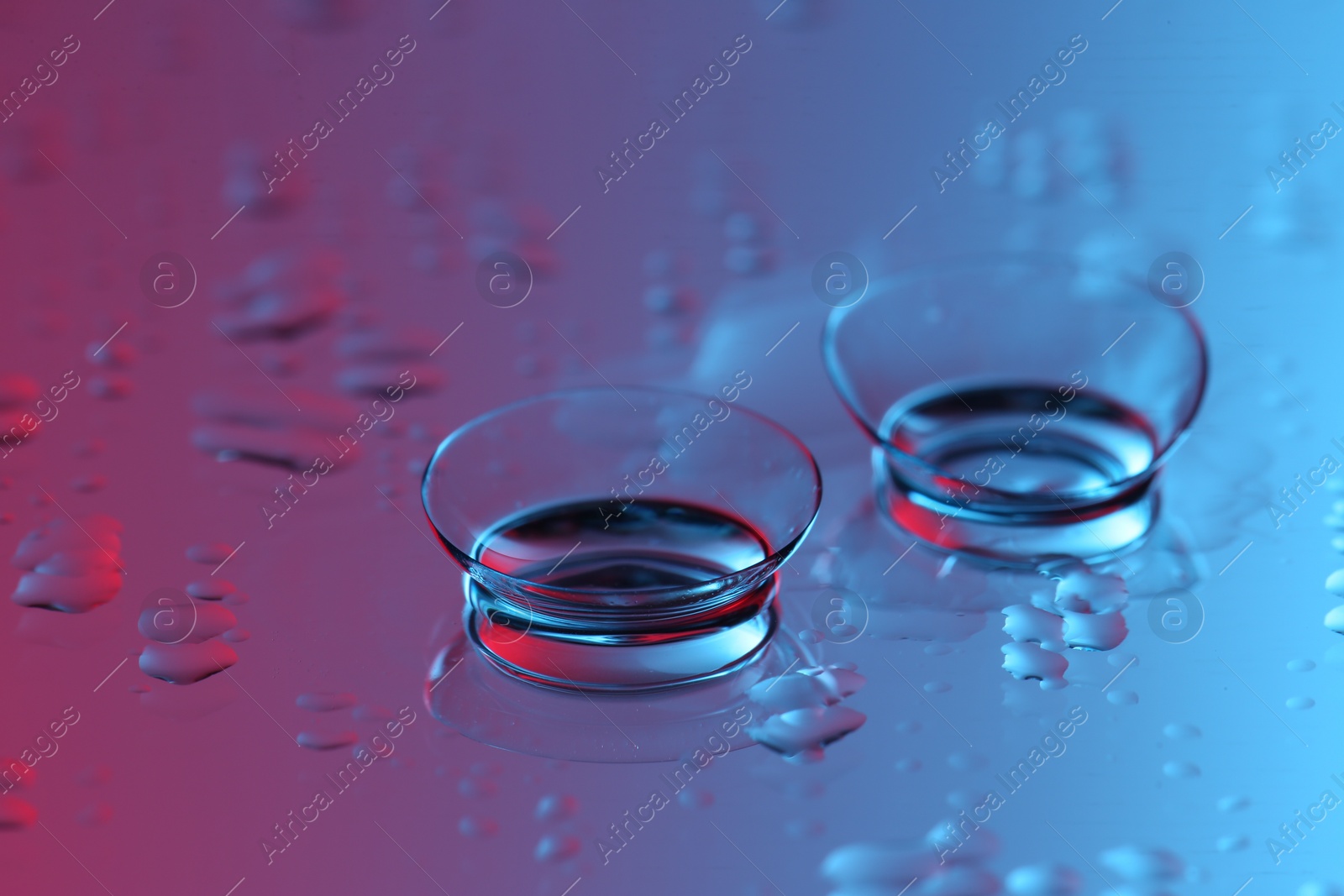 Photo of Pair of contact lenses on wet mirror surface, closeup