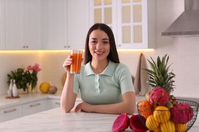 Young woman with glass of juice and exotic fruits in kitchen