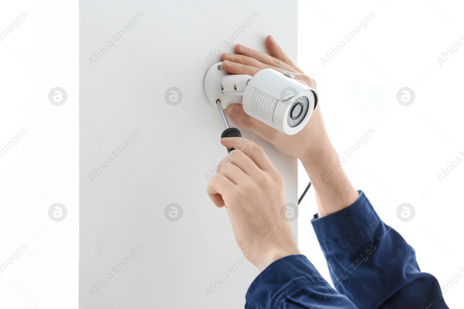 Photo of Technician installing CCTV camera on wall indoors, closeup