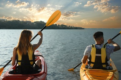 Photo of Couple in life jackets kayaking on river, back view. Summer activity