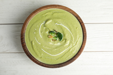 Photo of Delicious broccoli cream soup served on white wooden table, top view