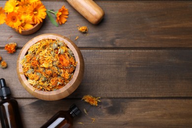 Dry calendula flowers and bottles of essential oil on wooden table, flat lay. Space for text