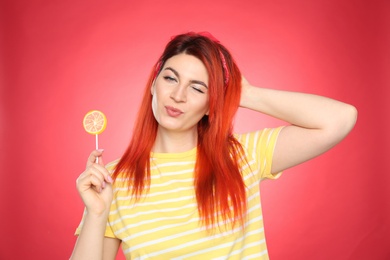 Photo of Young woman with bright dyed hair holding lollipop on red background
