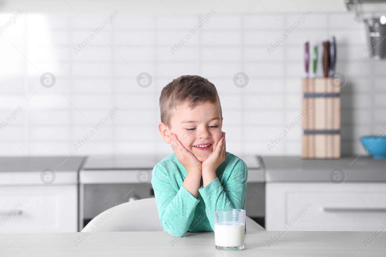 Photo of Cute little boy with glass of milk at table in kitchen