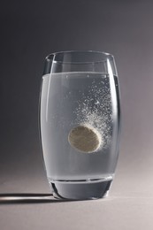 Effervescent pill dissolving in glass of water on grey background