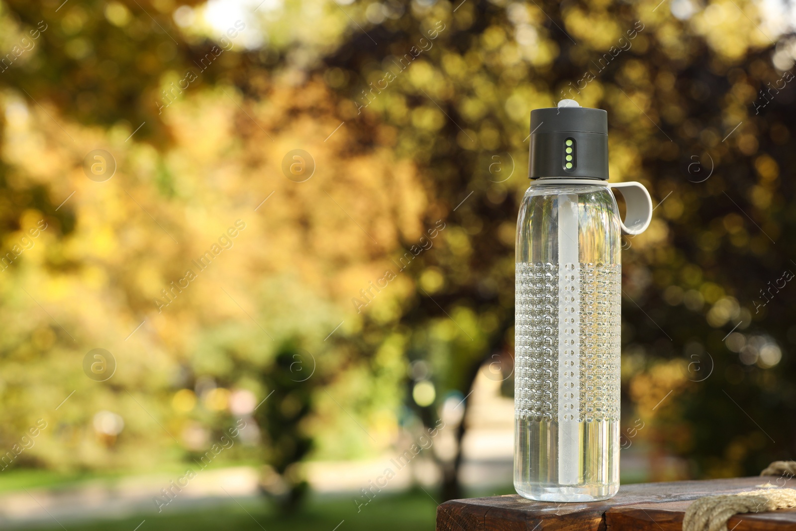 Photo of Sport bottle of water on wooden bench in park, space for text