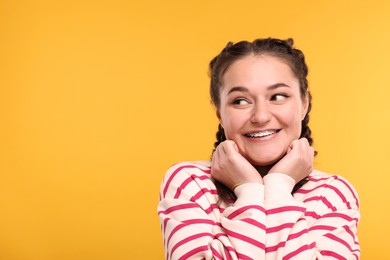 Photo of Smiling woman with braces on orange background. Space for text