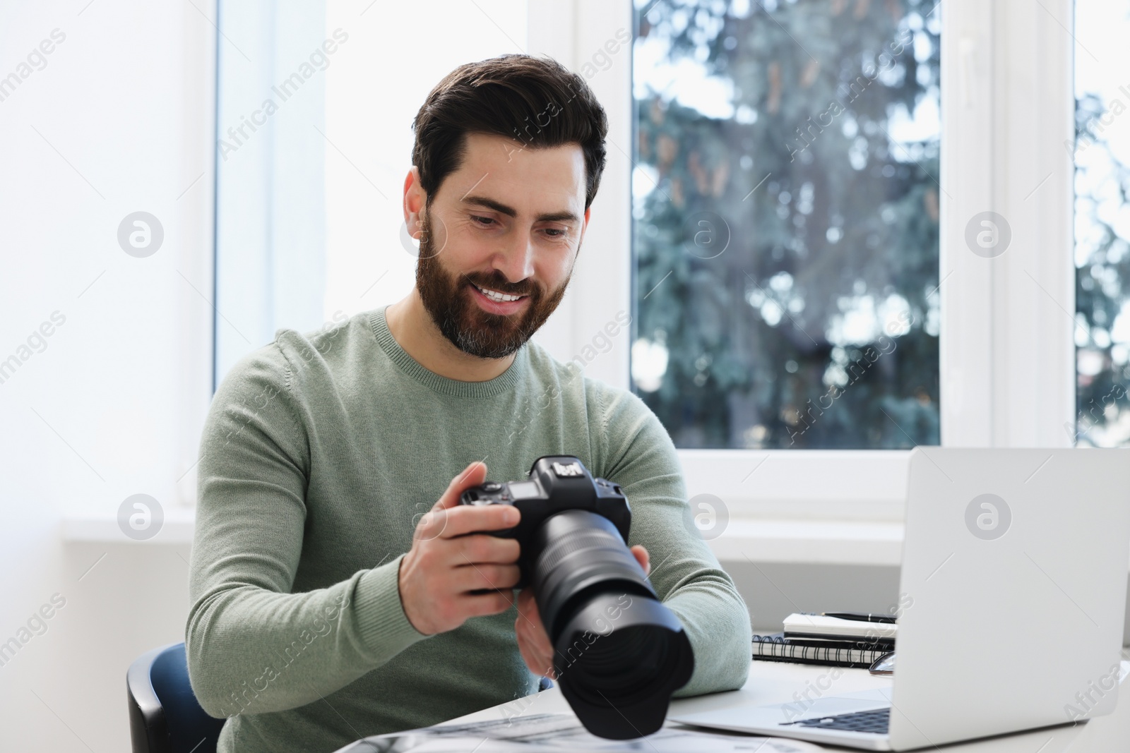 Photo of Professional photographer with digital camera at table indoors